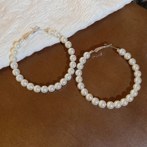 Detail of large hoop earrings with white pearls on a textured cream fabric background