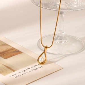 Detail of a golden waterdrop pendant with a white pearl on a sleek snake chain necklace