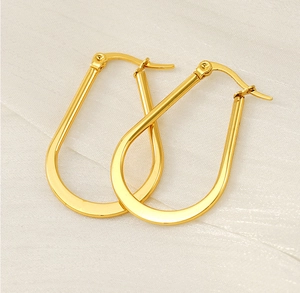 Detail of gold U-shaped earrings with polished finish on white textured silk fabric