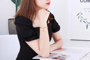 Elegant gold chain bracelet with clover pendant worn by a model in a natural setting