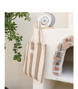 Detailed close-up of khaki striped canvas tote bag with SEASON 12 patch on brick wall