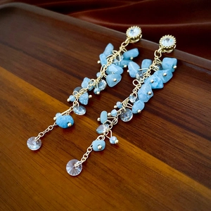 Détails macro de boucles d'oreilles bohèmes avec pierres bleu clair et chaîne dorée sur soie