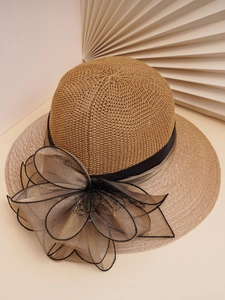 Detail of a beige woven sun hat featuring a large black organza flower and ribbon trim