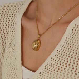 Elegant gold shell pendant necklace with twisted chain on model wearing beige sweater