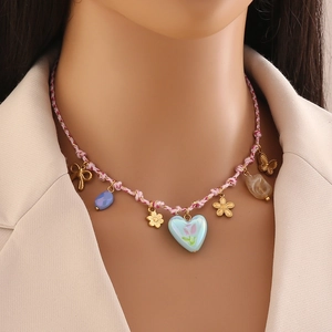 Détail du collier de plage tressé avec breloques dorées, gemmes et pendentif cœur tulipe
