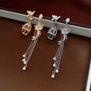 Detail of asymmetric birdcage earrings with pearls and long tassels in gold and silver