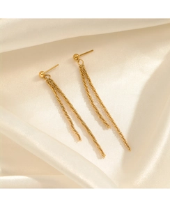 Macro view of long gold tassel earrings on beige satin fabric showing elegant chain detail