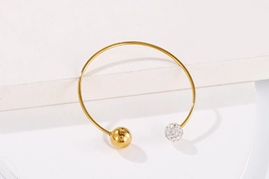 Détail d'un bracelet ouvert doré avec une boule en or poli et une boule pavée de cristaux