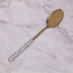 Golden stainless steel spoon with rhinestone handle on marble surface detail