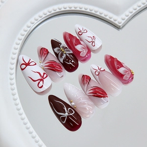 Handmade 3D floral almond press-on nails with red bows and pearl accents on mirror tray