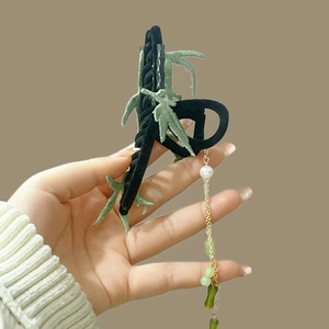 Close-up of bamboo tassel hair clip with green leaf embroidery and pearl accents