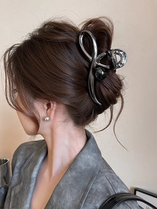 Detailed close-up of a large gunmetal hair claw clip with a black pearl on gray suit