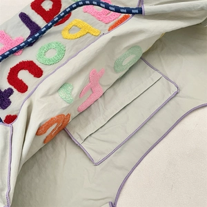 Close-up of canvas tote bag interior showing inner pocket and colorful letter embroidery