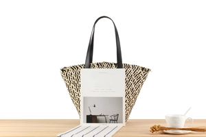 Detail of mixed color woven straw tote bag with black handles on a wooden table