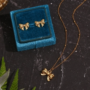 Detail of 18K gold-plated bow jewelry set with bead chain on elegant dark velvet