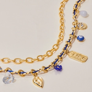 Detail of layered gold necklaces with blue beads, sun tag, and bohemian heart charms
