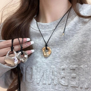 Detail of silver fluid heart pendant on black cord shown on a grey hoodie