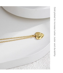 Detail of gold plated heart necklace with feather texture on white geometric steps