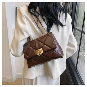 Detail of brown quilted chain bag with gold metal clasp on a white suit model