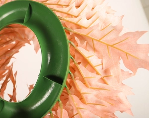 Close-up of pink artificial leaves attached to the green plastic frame of a Christmas wreath