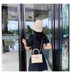 Model trägt beige gewebte Box-Tasche mit Kettengurt vor modernem Glasgebäude