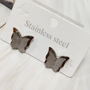 Macro detail of silver butterfly stud earrings in frosted stainless steel on a card