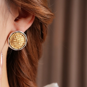 Detail of silver hoop earrings with a textured golden inner disc on a model's ear