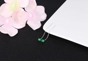 Macro shot of silver drop earrings with green zircons on white plate with flowers