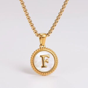 Detail of a golden round pendant with shell inlay featuring an embossed letter F on top