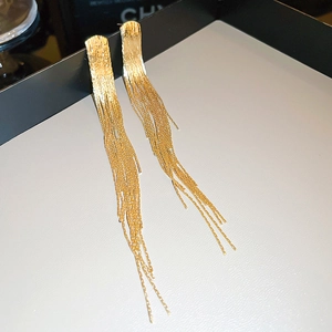 Detailed view of long gold tassel earrings with metallic texture on a tray