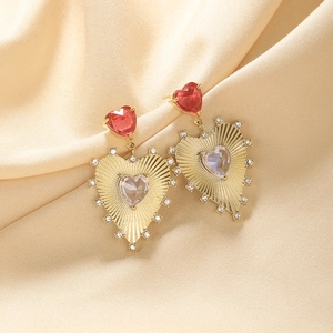 Macro shot of gold-plated heart earrings with red and clear zircon on silk fabric