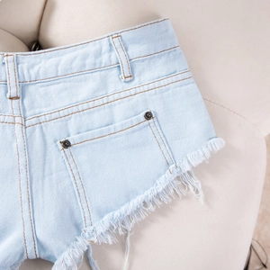 Detail von hellblauen Denim-Shorts mit ausgefransten Säumen und Metallnieten-Akzenten
