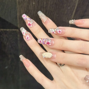 Dettaglio di unghie ballerina con fiori viola, perle e strass luccicanti