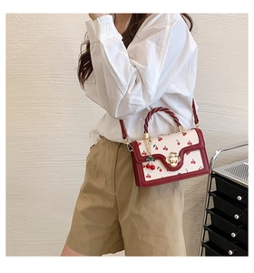 Detail of canvas crossbody bag featuring red cherry print and woven rope handle