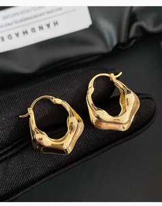 Gros plan détaillé de boucles d'oreilles dorées ondulées sur tissu texturé sombre