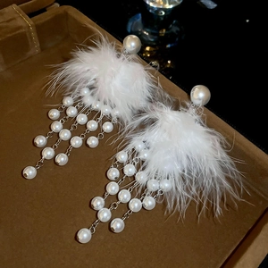 Close-up of elegant white feather and faux pearl tassel earrings in a brown velvet box