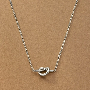 Silver knotted heart pendant necklace in titanium steel on a brown textured background