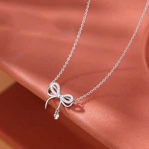 Elegant silver bow pendant necklace with sparkling zircon stones on an orange background