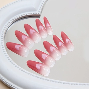 Pink gradient long almond press-on nails with glitter heart patterns on a mirror surface