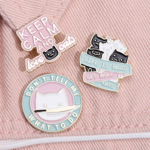 Three creative enamel cat brooches with slogans on pink denim fabric background