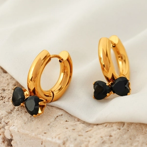 Golden hoop earrings with black heart-shaped stone bow design on stone background