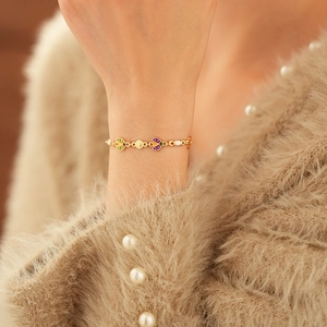 Détail d'un bracelet vintage doré avec breloques en émail coloré sur une manche en maille