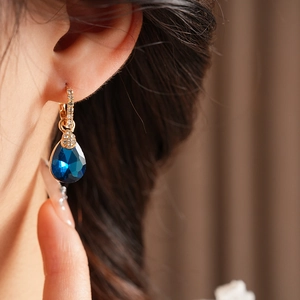 Gros plan de créoles vintage dorées avec cristal bleu en forme de goutte sur un modèle