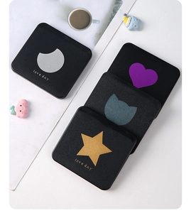 Flat lay of four black compact mirrors with silver moon, heart, cat, and star foil patterns