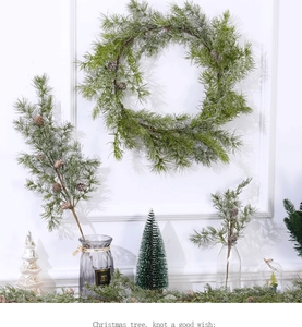 Close-up of green snowflake pine wreath and mini Christmas trees on white wall