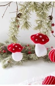 Red flocked mushroom Christmas ornament hanging on a pine tree branch with pinecones
