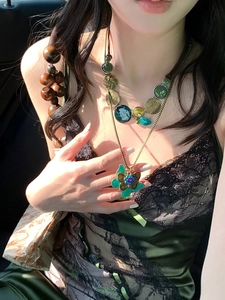 Detail of layered vintage bronze necklace featuring green butterfly and coin charms