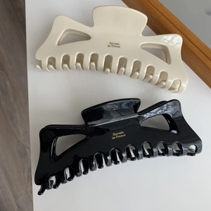 Détail de grandes pinces à cheveux noir et crème avec lettrage doré Barrette La France