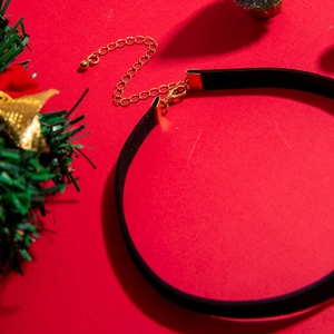 Detail of black velvet choker with gold lobster clasp on festive red background