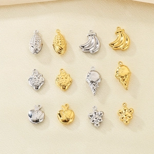 Flat lay macro of 3D stainless steel fruit charms including corn and apple in gold and silver